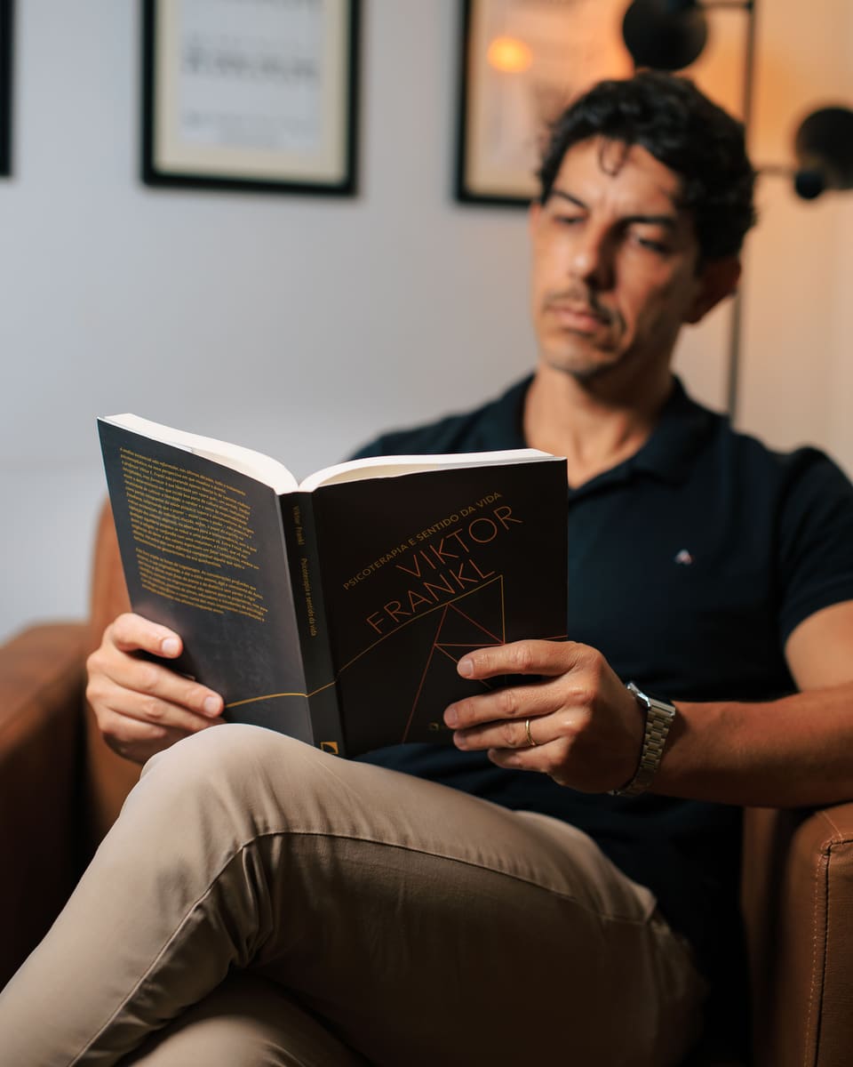 Fred Dias lendo o livro Psicoterapia e sentido da vida, de Viktor Frankl, sentado em uma poltrona.