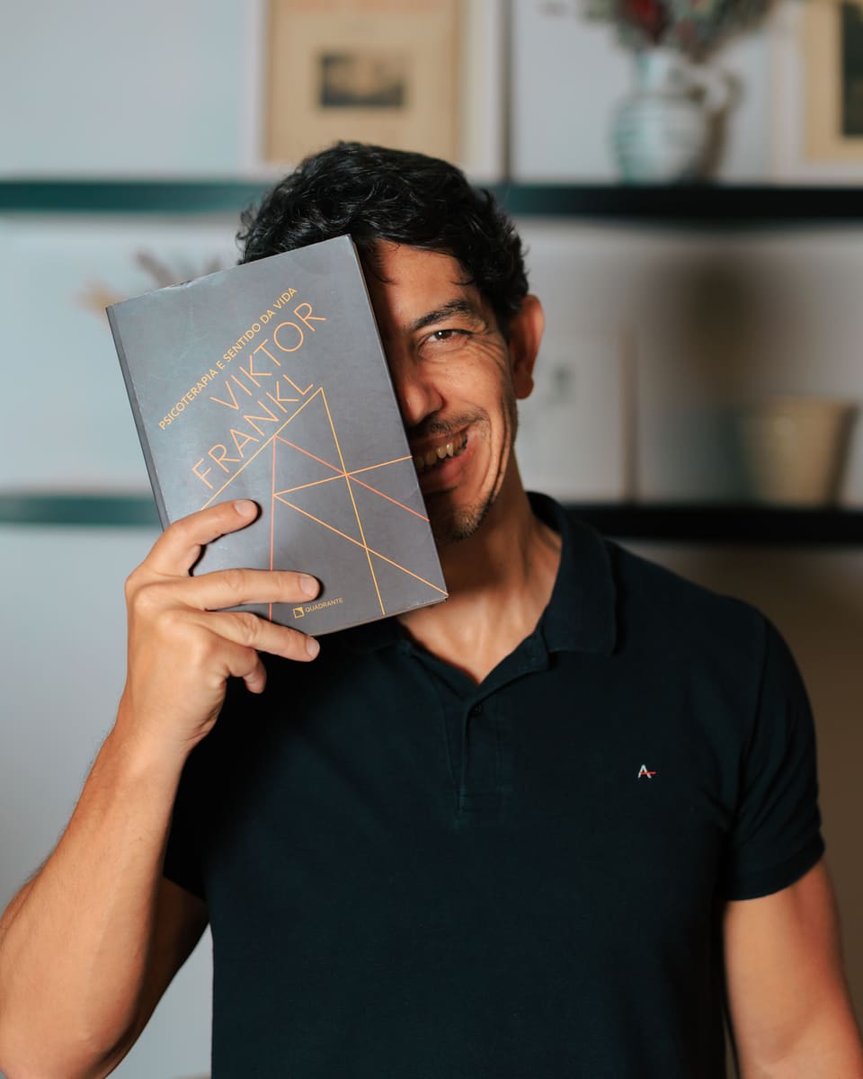 Fred Dias sorrindo, com o livro Psicoterapia e sentido da vida, de Viktor Frankl, cobrindo metade do rosto.