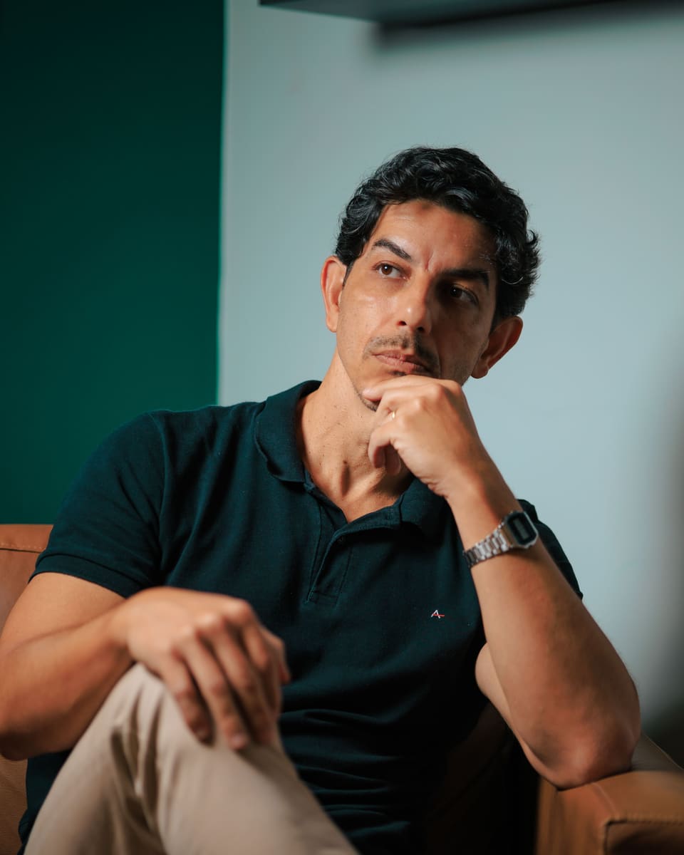 Fred Dias sentado em uma poltrona, com a mão no queixo e postura tranquila, em um consultório de paredes claras e verde-garrafa.